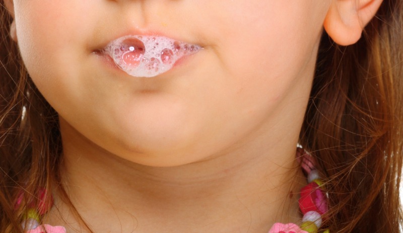 Nahaufnahme eines Kindes mit schäumendem Speichel an den Lippen. Das Kind hat braune Haare und trägt eine bunte Halskette.